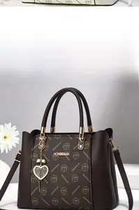 Détail d'un sac à main marron en cuir avec imprimé monogramme et pendentif en cœur