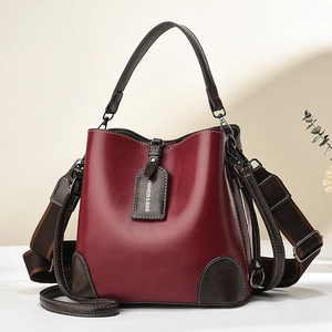 Minimalistische tiefrote Eimertasche mit braunem Lederbesatz und breitem Schultergurt