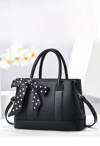 Détail d'un sac seau noir en cuir grainé avec foulard à pois sur un support de présentation