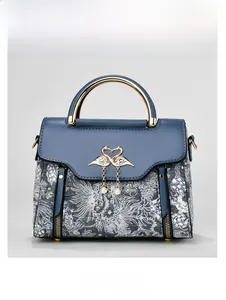 Detail of blue and white patterned handbag with golden swan buckle and pearl pendant