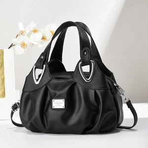 Sac à main plissé noir élégant avec boucles argentées et bandoulière sur table blanche