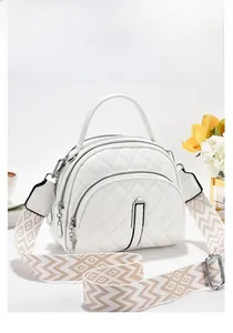 Detailed view of white quilted crossbody bag featuring triple zippers and patterned strap