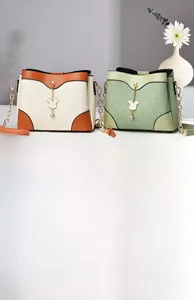 Detail of pleated shoulder bags in cream and green with metal chains and rabbit charms