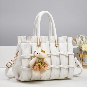 Close-up of white woven leather handbag featuring a plush bear charm and gold hardware