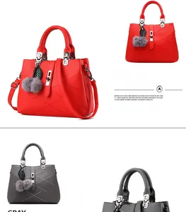Detailed view of leather handbag with metal lock and decorative charms in red and grey