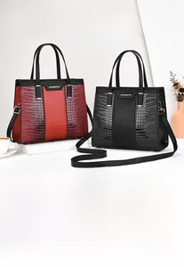 Close-up of burgundy and black Kelly bag with crocodile pattern and gold-tone hardware