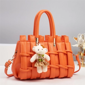 Detail of orange litchi grain leather tote with woven texture and teddy bear charm