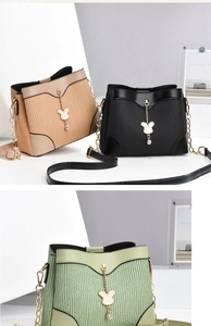 Close-up of pleated bucket bags in beige, black, and green with gold rabbit chain charms