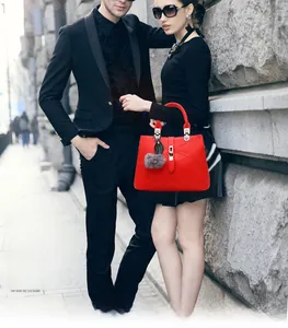 Detail of red embossed leather handbag with grey pompom charm and metal lock closure