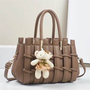 Detail of brown litchi pattern leather bag with woven design and teddy bear charm