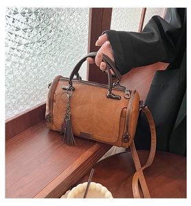 Detailed view of vintage brown leather Boston bag with decorative tassel on wooden background