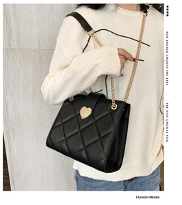 Detail of quilted leather texture and golden heart metal lock on a black shoulder bag