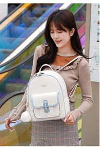 Detail of white PU leather backpack with blue trim and plush charm worn by model