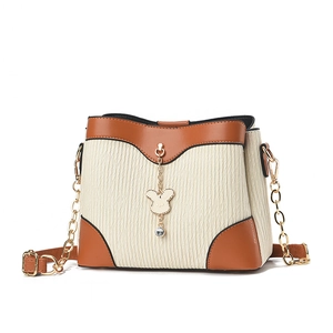 Minimalist bucket bag in off-white textured fabric with brown trim and rabbit pendant