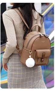 Detail of dark brown faux leather backpack with metallic buckle and white fur ball pendant