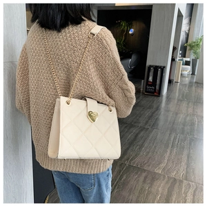 Detailed close-up of beige quilted shoulder bag with gold heart-shaped metal lock