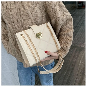 Close-up of cream quilted tote bag featuring golden heart-shaped clasp and chain strap