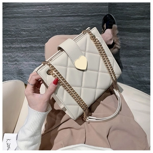 Detailed macro of a quilted beige chain bag featuring a gold heart-shaped metal lock