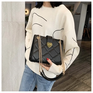 Close-up of black quilted leather shoulder bag featuring a gold heart-shaped metal clasp