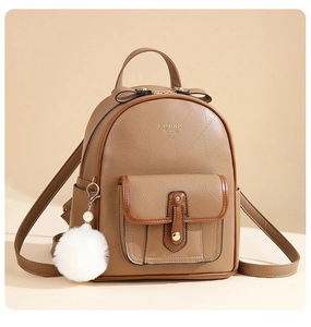 Close-up of brown textured leather backpack detail with golden buckle and white fur charm