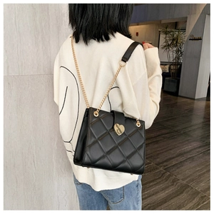 Detail view of a black quilted shoulder bag with gold heart clasp and chain strap