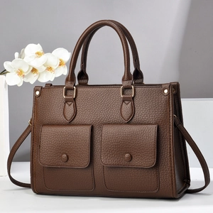 Detailed view of brown lychee leather handbag with front pockets and gold hardware