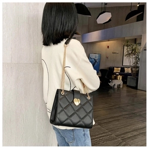 Detail of black quilted shoulder bag featuring gold heart lock and elegant chain strap