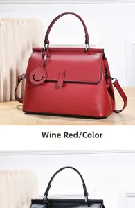 Detail der weinroten Handtasche aus genarbtem Leder mit rundem Anhänger auf Holz