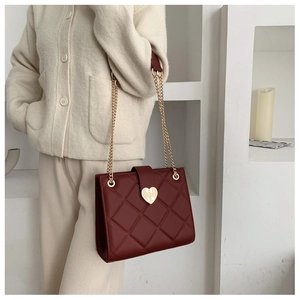 Detail of burgundy tote bag with quilted pattern and gold heart lock shown on model