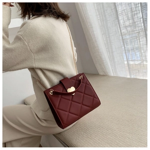 Detail of burgundy quilted tote with gold heart lock and chain strap on shoulder