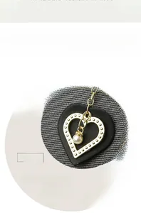 Detail of heart-shaped leather bag charm with gold metal frame and dangling pearl
