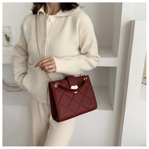 Detail of red quilted shoulder bag featuring a gold heart clasp on a stylish knit outfit
