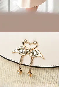 Détail du fermoir cygne doré avec cristal coeur et perle sur un petit sac à main beige