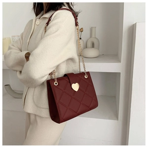 Detail of red quilted shoulder bag featuring a gold heart-shaped lock and chain strap