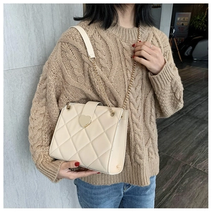 Detailed shot of cream quilted shoulder bag featuring a gold heart-shaped metal buckle