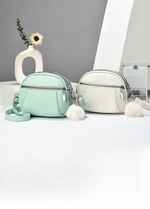 Detail of lychee textured PU leather crossbody bag with multiple zippers and pompom charm