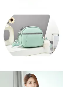 Detail of mint green triple-zipper crossbody bag with litchi texture and plush pompom