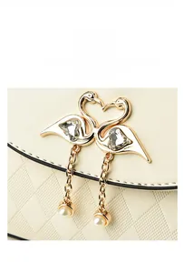 Detailed view of beige leather bag with swan heart hardware and pearl chain pendant
