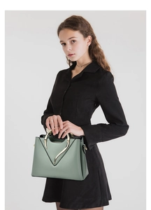 Détail du sac seau en cuir vert clair avec poignée en métal doré porté par mannequin