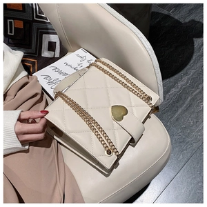 Detailed shot of beige quilted crossbody bag featuring a golden heart-shaped metal clasp
