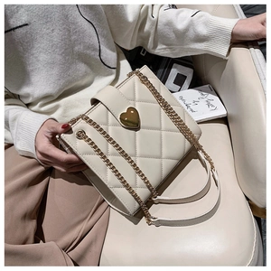 Close-up of cream white quilted shoulder bag with gold heart-shaped lock and chain