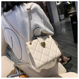 Detail of cream quilted crossbody bag with golden heart buckle and chain strap