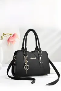 Close-up of black lychee grain leather handbag with gold heart charm and pearl detail