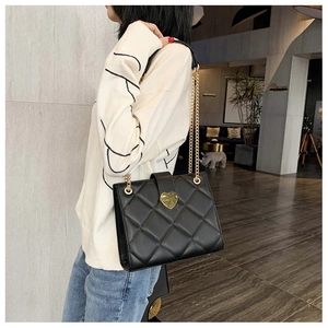 Close-up of black quilted leather shoulder bag featuring a gold heart-shaped metal buckle