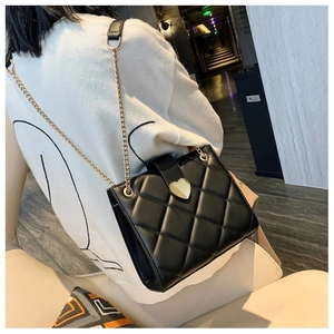 Detail of black quilted shoulder bag featuring gold heart lock and chain strap