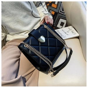 Detail of black quilted shoulder bag featuring gold heart clasp on a white sofa