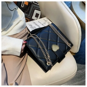 Close-up of black quilted shoulder bag featuring a golden heart-shaped lock and chain strap