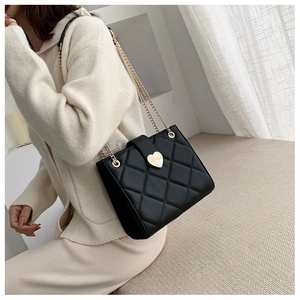 Detail view of black quilted leather shoulder bag with gold heart clasp on a model