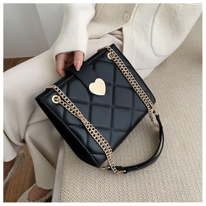 Detail of black quilted shoulder bag featuring a gold heart-shaped metal lock and chain strap