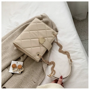 Detail of cream quilted crossbody bag with golden heart clasp and chain strap